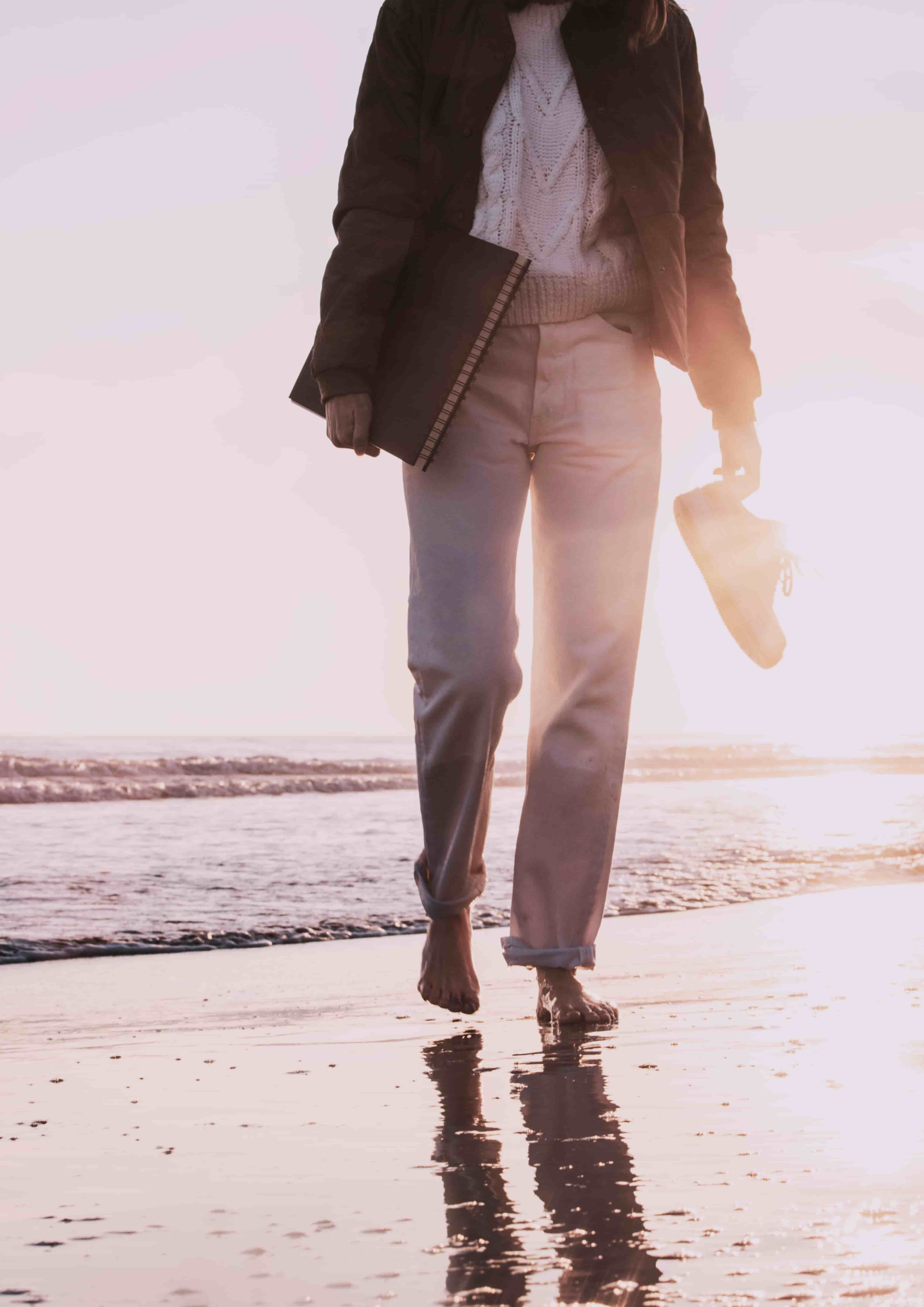 Person walking on beach at sunset with journal